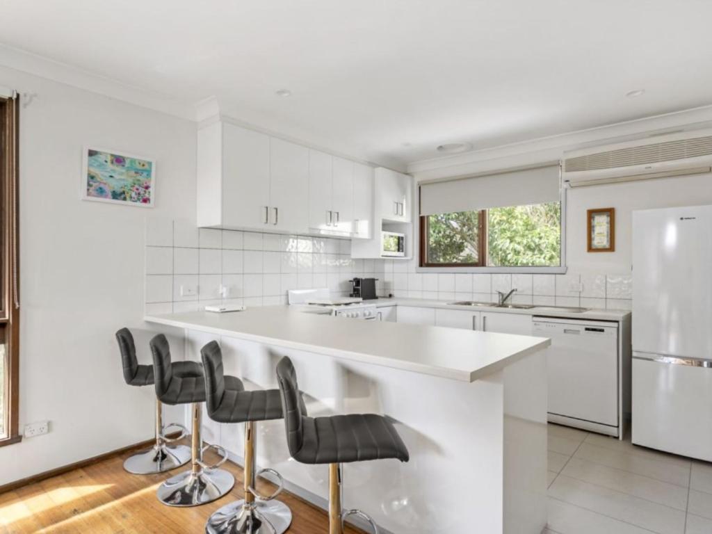 a white kitchen with a large white counter and stools at Neat And Sweet Blairgowrie Retreat in Blairgowrie