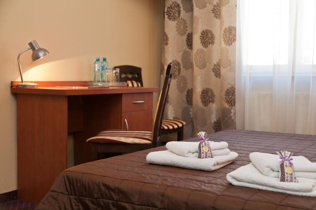 a room with a bed with towels and a desk at Hotel Maksymilian in Krakow