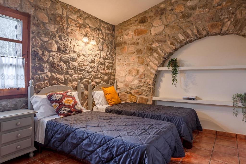 - une chambre avec 2 lits et un mur en pierre dans l'établissement Can Torrotes, à La Vall de Bianya