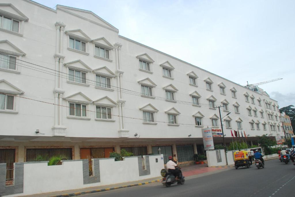 班加羅爾的住宿－帕萊阿塔關口酒店，一座白色的大建筑,前面有骑摩托车的人