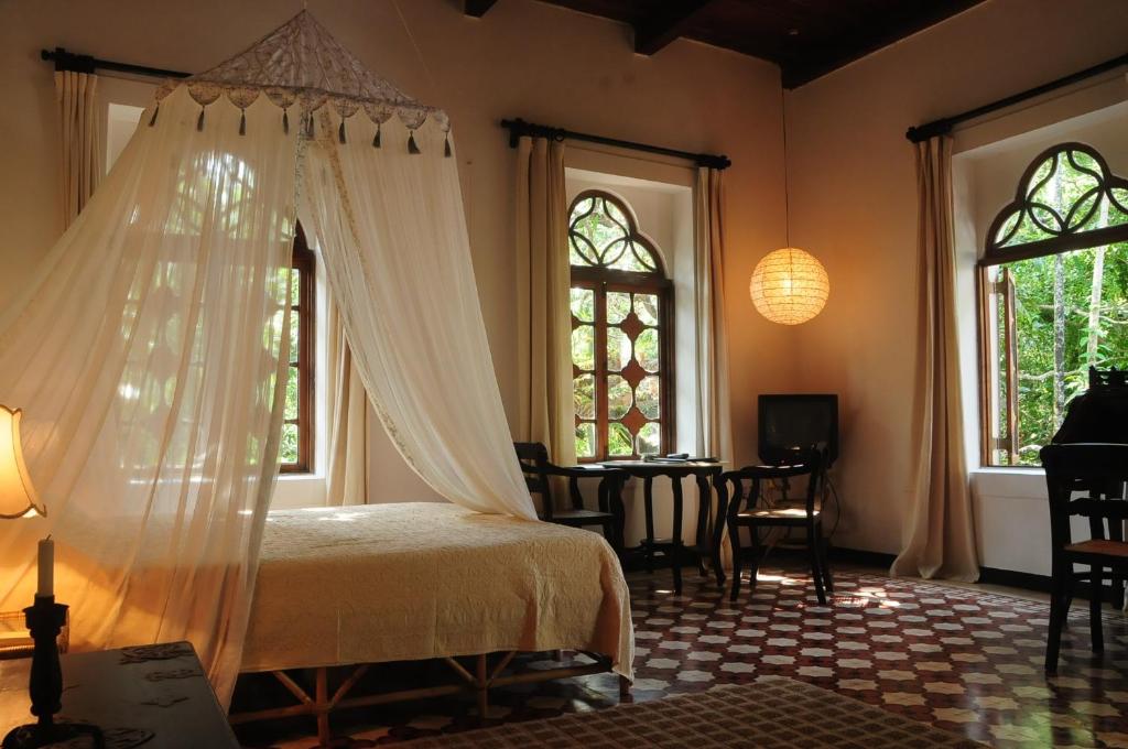 a bedroom with a bed and a table and windows at Marbella Guest House in Sinquerim