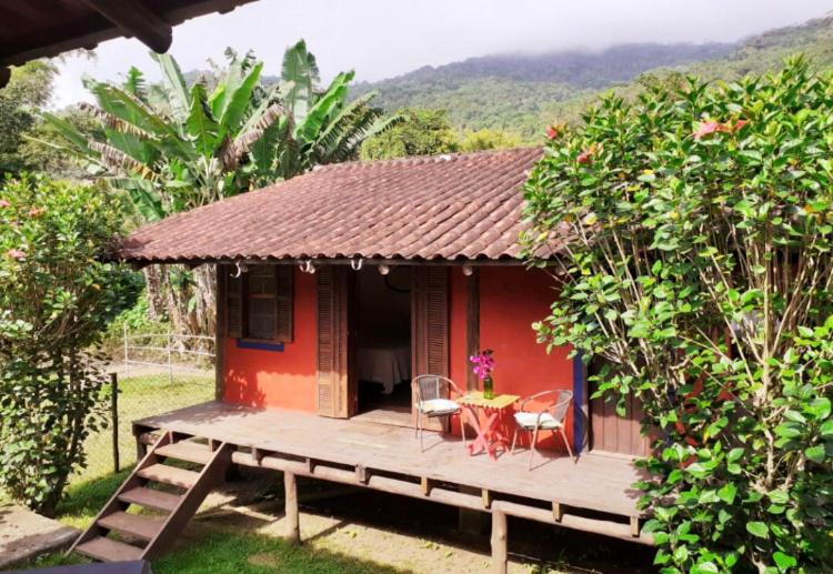 uma pequena casa vermelha com uma mesa e cadeiras num deque em Cabana Lua - Praia de Castelhanos em Ilhabela
