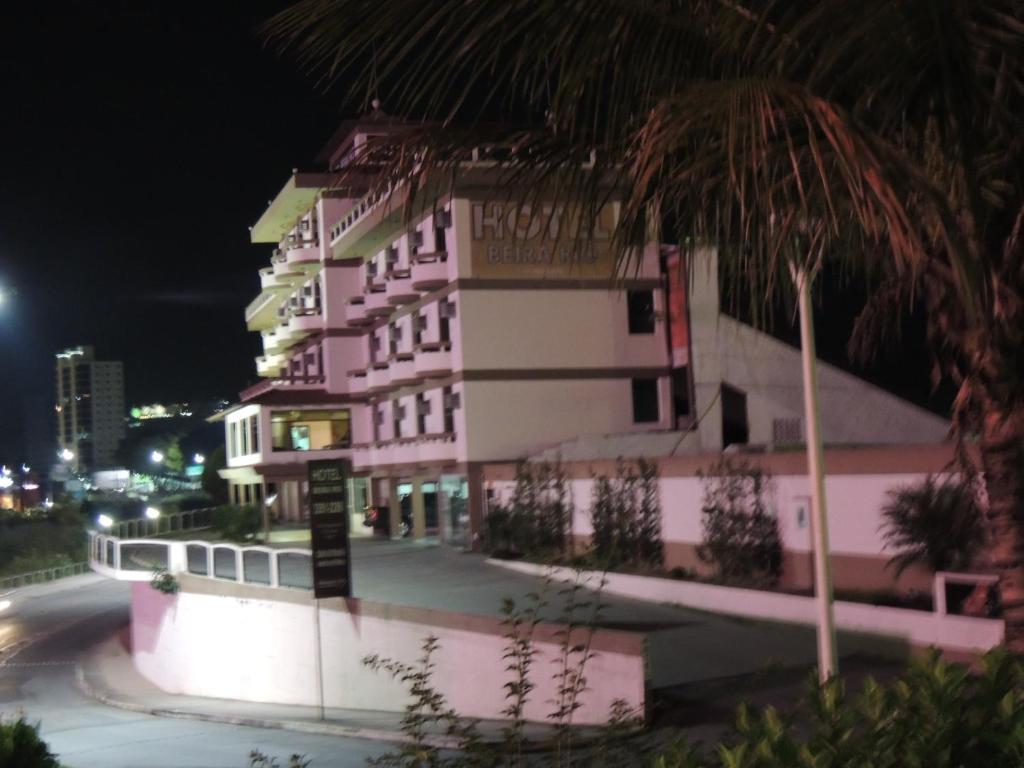 ein rosa und weißes Gebäude in der Nacht mit einer Palme in der Unterkunft Hotel Beira Rio in Brusque