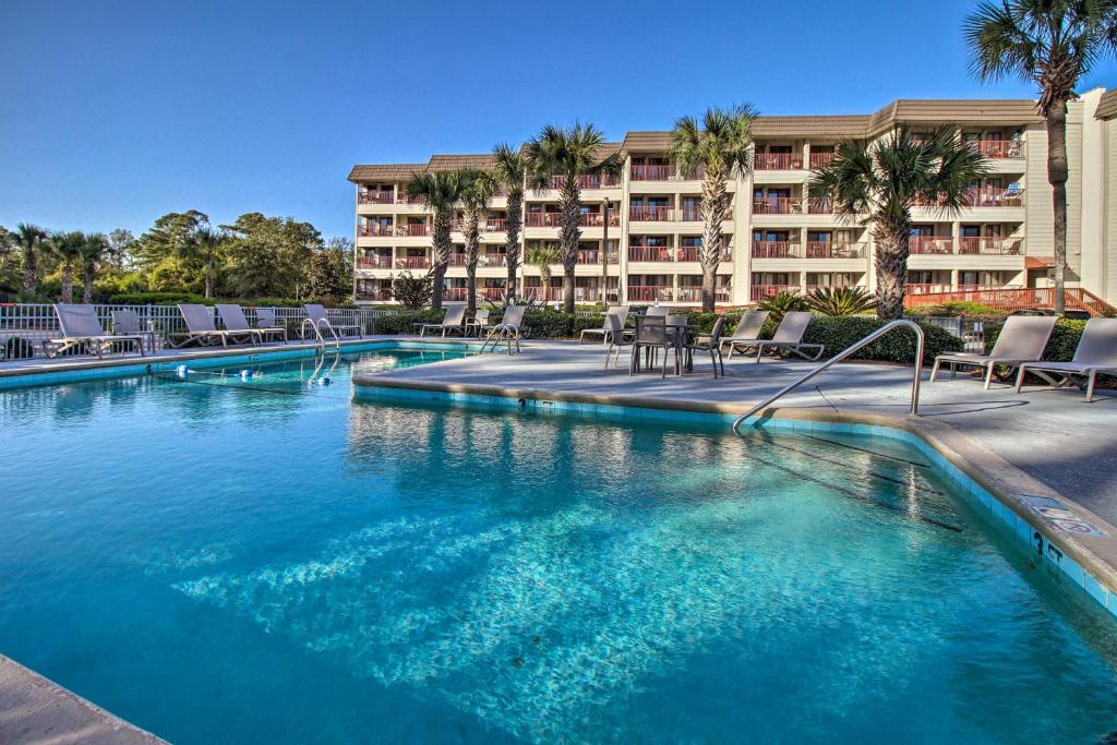 a large swimming pool with chairs and a hotel at Hilton Head Condo with Balcony and Pool, Walk to Beach in Hilton Head Island