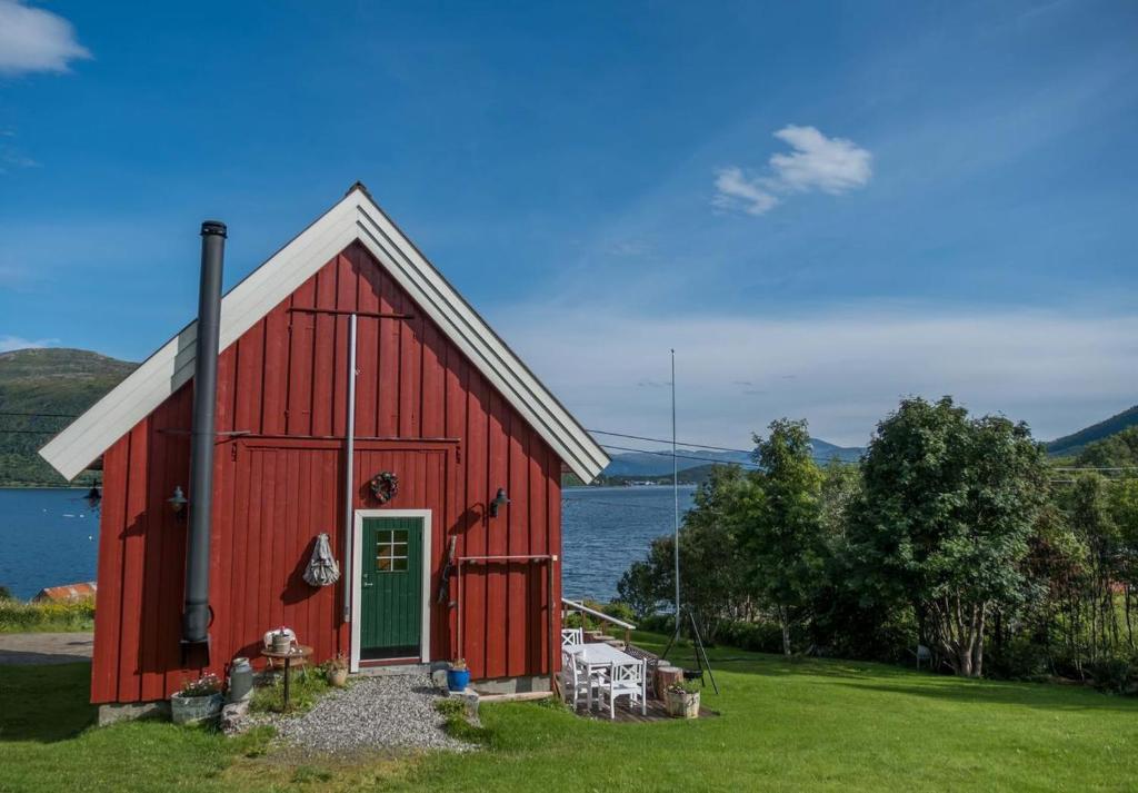czerwona stodoła z zielonymi drzwiami obok wody w obiekcie Kræmarvika Lodge w mieście Tromsø