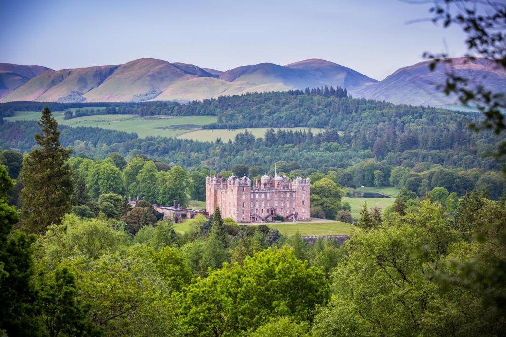 a castle in the middle of a forest with mountains at Stableyard Apartment: Drumlanrig Castle in Thornhill