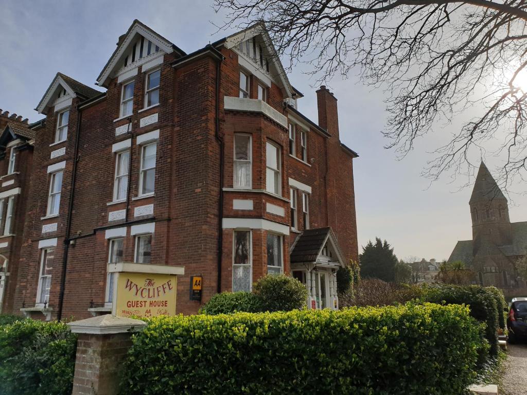 un grand bâtiment en briques avec un panneau devant lui dans l'établissement The Wycliffe, à Folkestone