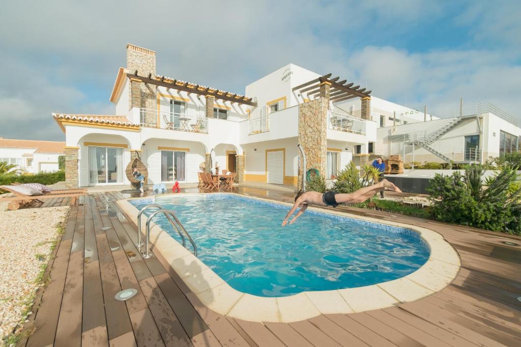 a man jumping into a swimming pool in front of a house at Arrifana Destination Suites in Aljezur