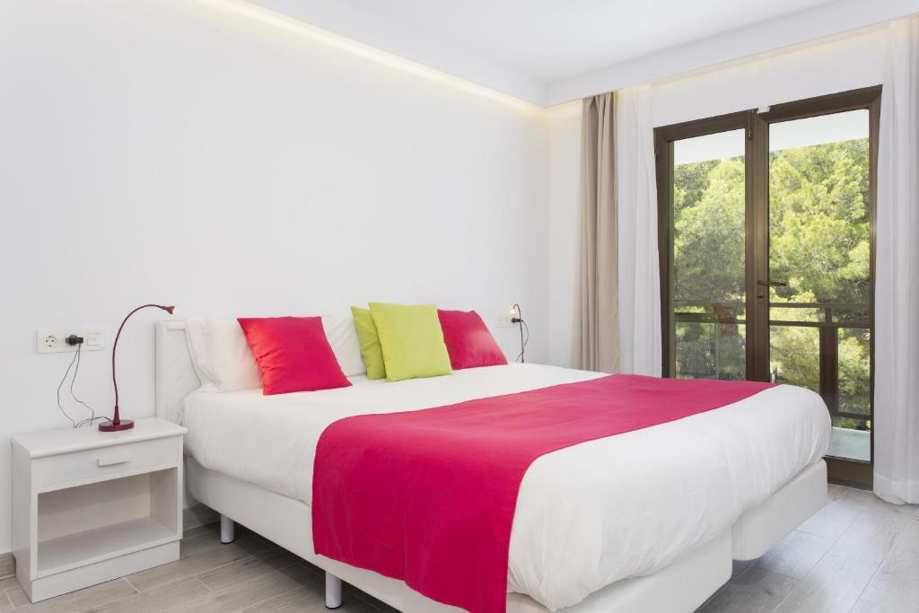 a white bedroom with a large bed with colorful pillows at Guya Wave Hotel in Cala Ratjada