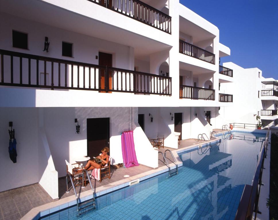 a woman sitting next to a swimming pool next to a building at Hersonissos Maris in Hersonissos