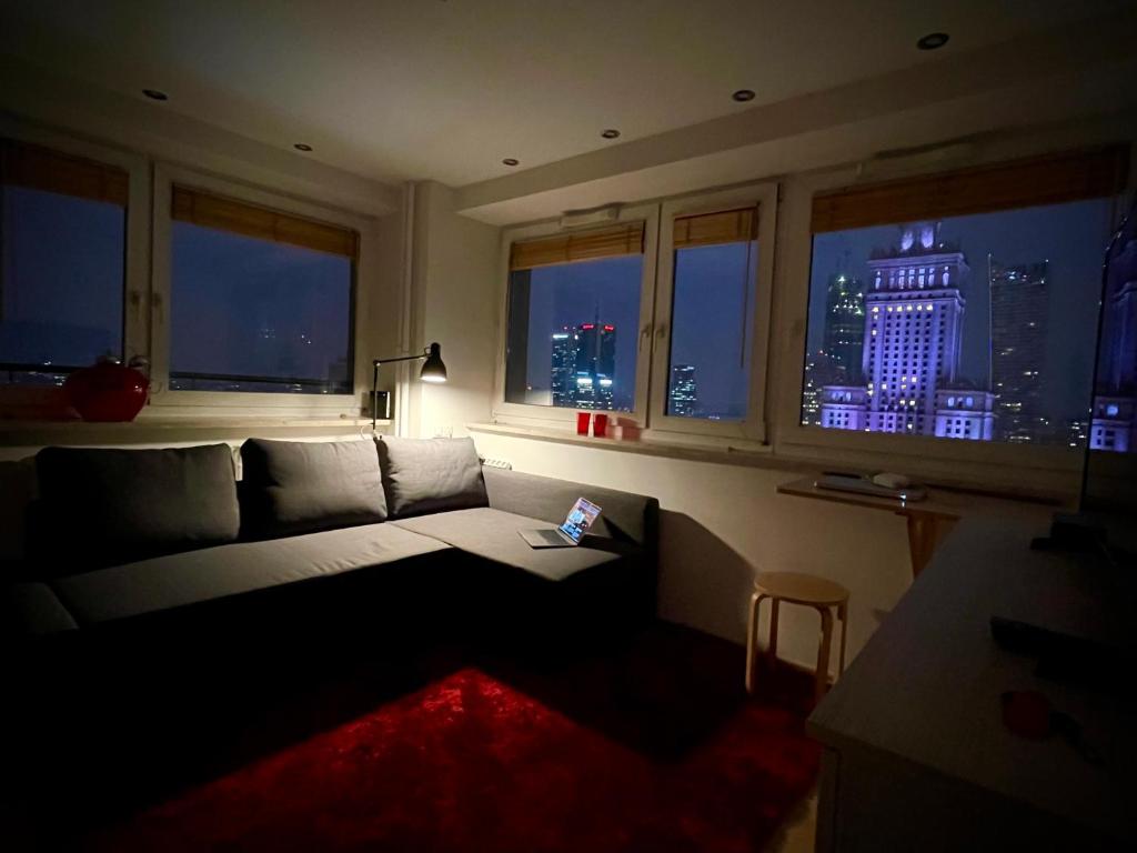 ein Wohnzimmer mit einem Sofa und Fenstern mit Blick auf die Skyline der Stadt in der Unterkunft Super Apartament RED Centrum Best View in Town 2x Metro Fast WiFi 300 Mbs Netflix AppleTV SmartTV Spotify Panorama Miasta in Warschau