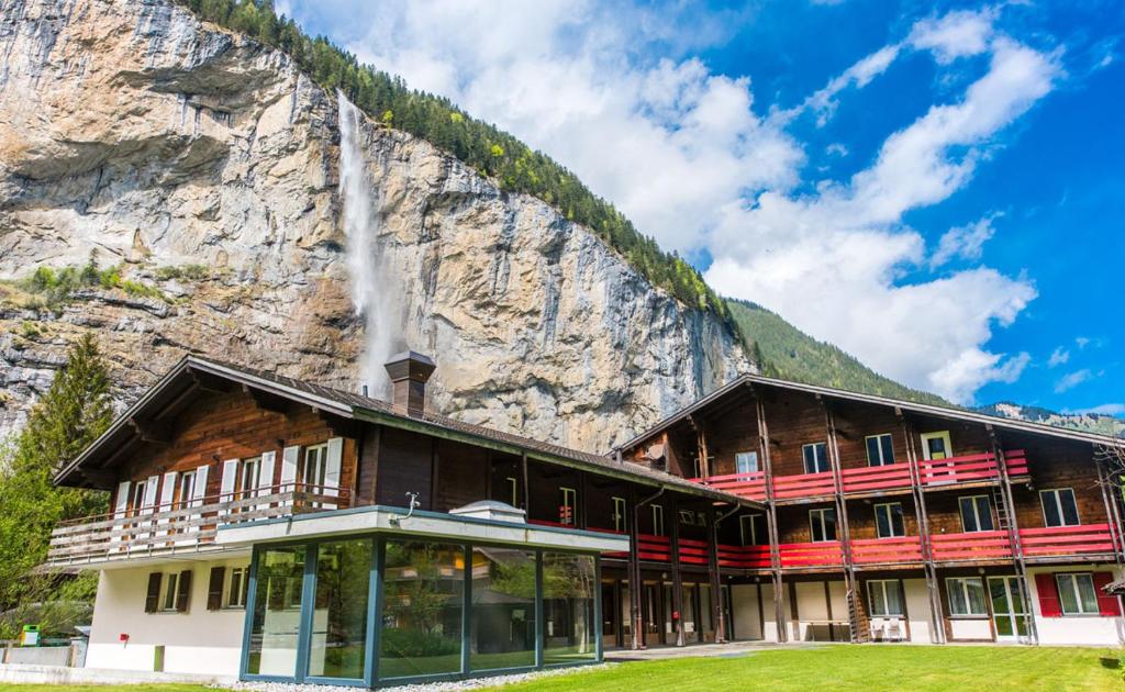 a building in front of a mountain with a waterfall at Alpine Base Hostel - Adults only in Lauterbrunnen