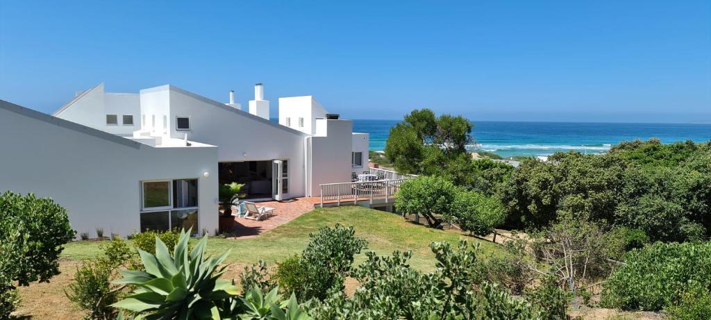 ein weißes Haus mit dem Ozean im Hintergrund in der Unterkunft Southern Cross Beach House in Groot Brak Rivier