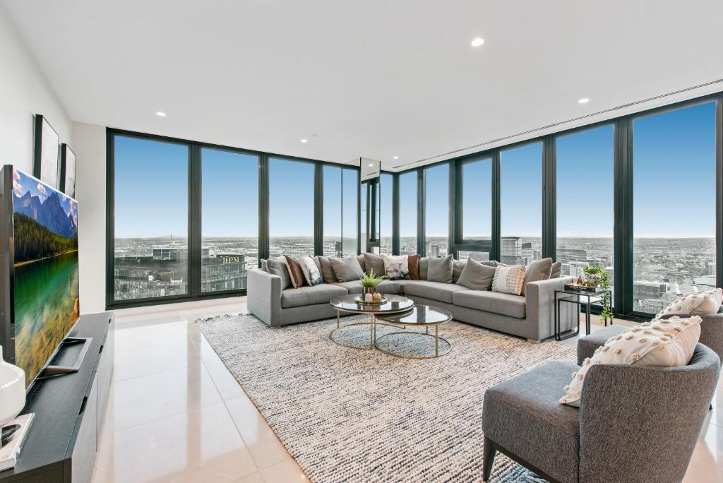 sala de estar con sofás, TV y ventanas grandes. en Melbourne City Apartments Panoramic Skyview Penthouse en Melbourne