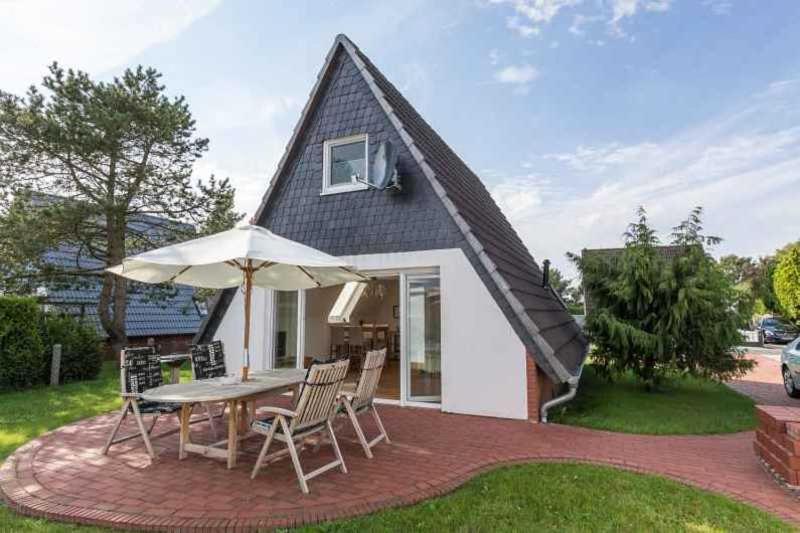 ein Haus mit einem Tisch, Stühlen und einem Sonnenschirm in der Unterkunft Ferienhaus Boje 9 in Neuharlingersiel