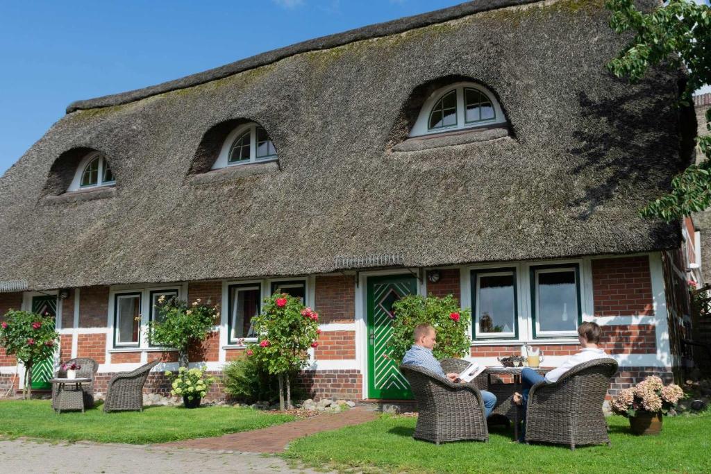 two people sitting at a table in front of a thatched house at Ferienwohnungen von Schassen in Twielenfleth