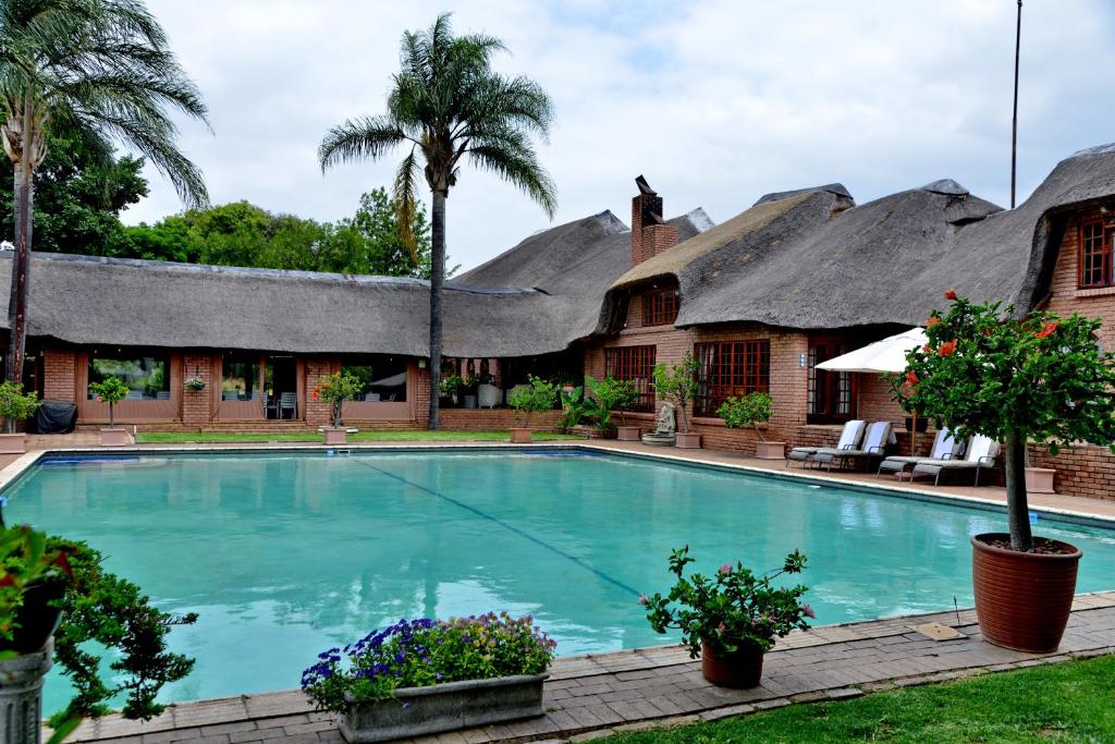 a swimming pool in front of a house with thatched roofs at Owls Loft Guest House in Midrand
