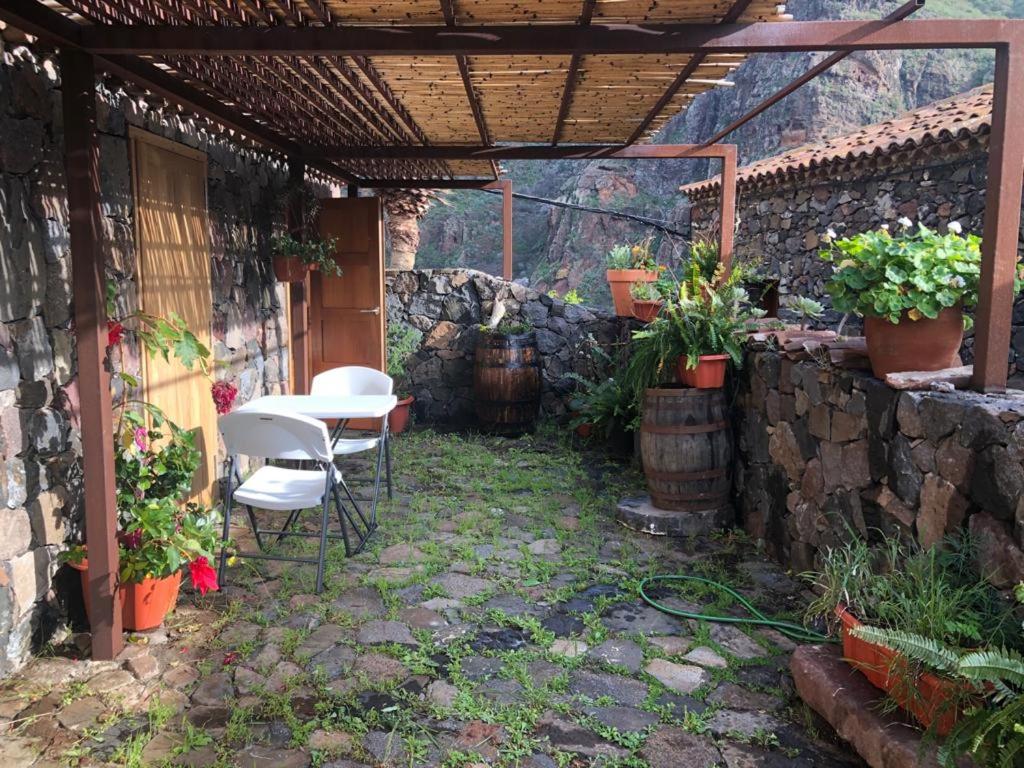 un patio con mesa, sillas y pared de piedra. en Casa Rural El Horno Masca, en Buenavista del Norte