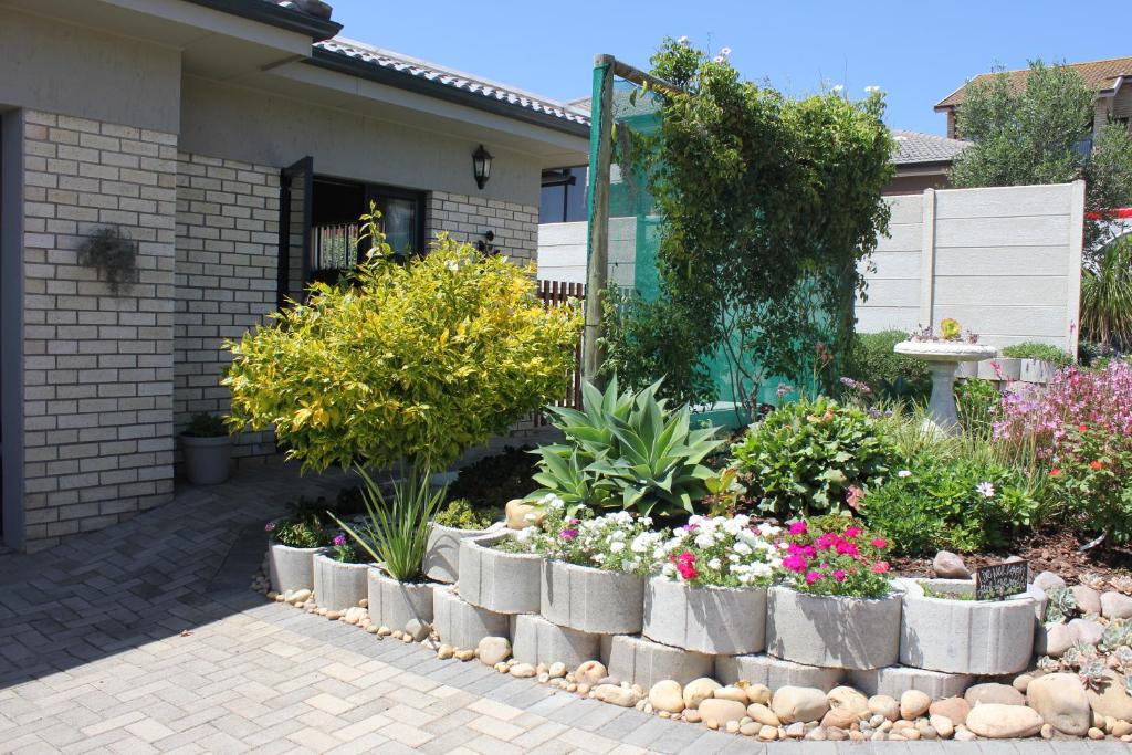 um jardim com flores e plantas em frente a uma casa em Traveller's Rest, Reebok em Mossel Bay