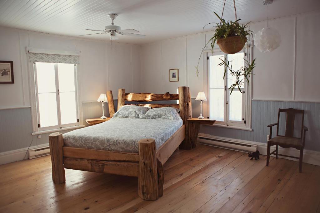 a bedroom with a wooden bed and two windows at Auberge Carpe Diem in Baie-Saint-Paul