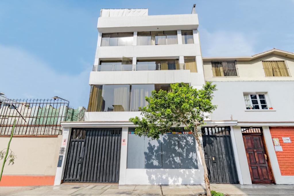 un edificio blanco con puertas negras y un árbol delante en INTI KILLA Hostel en Lima