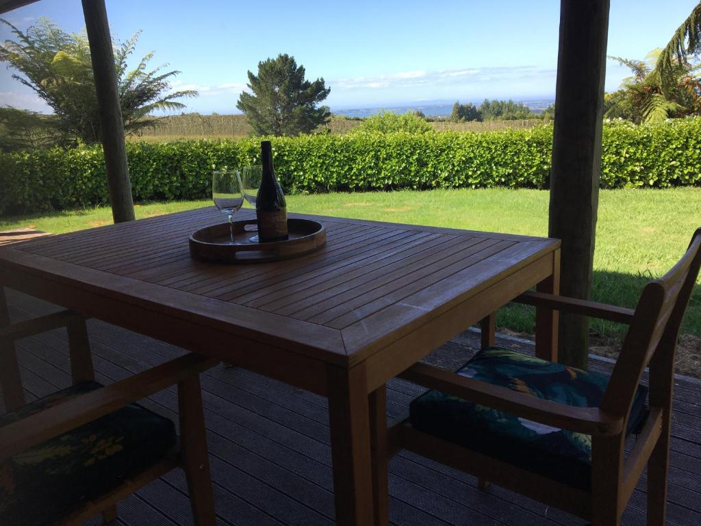 a wooden table with a bottle of wine and two chairs at Te Harinui - Peaceful rural escape in Tauranga