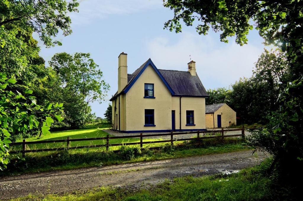 una vieja casa amarilla con dos chimeneas en un campo en The Gardener's Cottage, en Ballymote