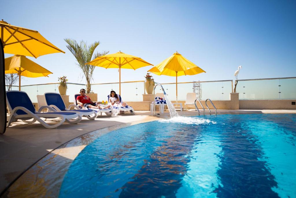 a swimming pool with people sitting on chairs and umbrellas at Holy Family Hotel in Jabal aţ Ţayr