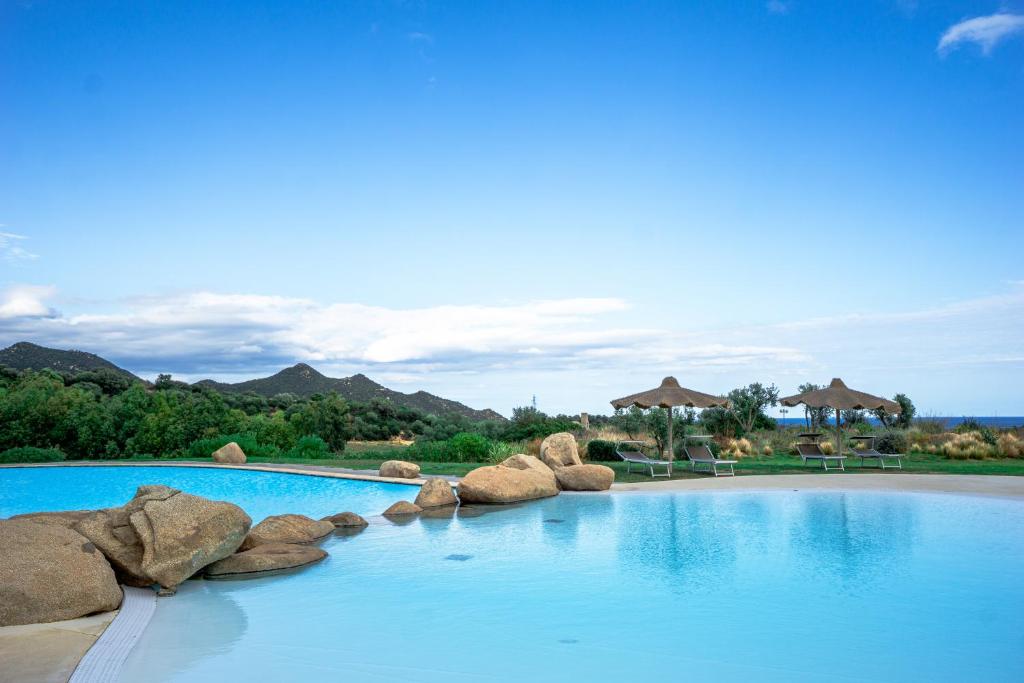 a swimming pool with blue water and rocks at BGItalianVacation - Ville Li Conchi in Castiadas