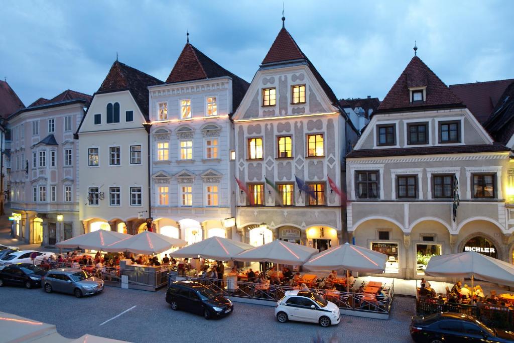 a group of buildings with tables and cars parked in a parking lot at Stadthotel Styria in Steyr