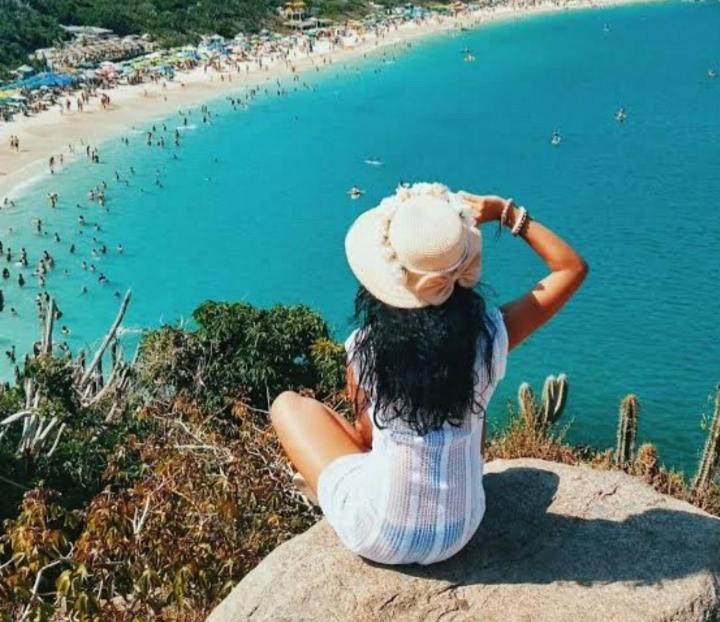 a woman sitting on a rock looking at a beach at Casa Jasmim arraial do cabo in Arraial do Cabo