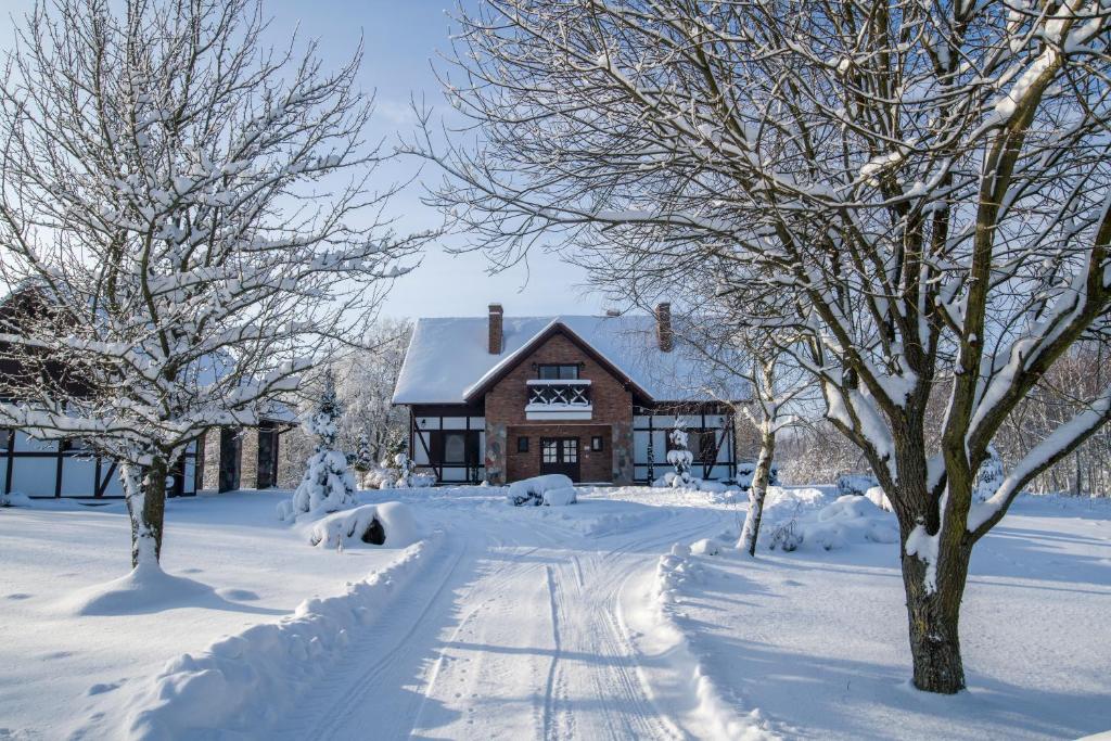 a house covered in snow with trees in the foreground at Hotel SPA Dr Irena Eris Wzgórza Dylewskie - Siedliska in Wysoka Wieś