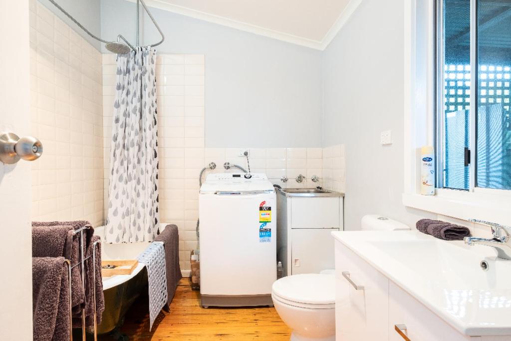 a white bathroom with a refrigerator and a toilet at Quartz Cottage Geelong in Geelong