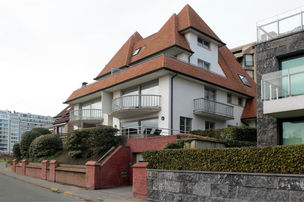 a white building with a brown roof on a street at Fairway Apartment in Knokke-Heist