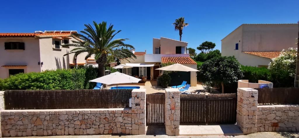 una casa con una valla, sombrillas y palmeras en Finca Ses Rotes en Cala Llombards