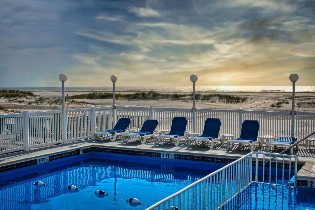 a swimming pool with lounge chairs and the beach at Acacia Beachfront Resort in Wildwood Crest