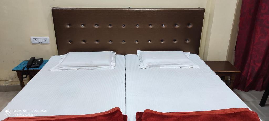 BalrāmpurにあるHotel Avadh Balrampurの白いシーツ2枚と茶色のヘッドボードが備わるベッド