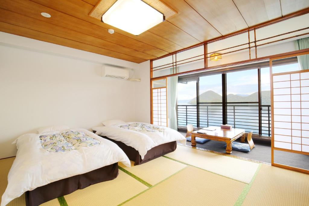 a bedroom with two beds and a table and windows at Toya-onsen Hotel Hanabi in Lake Toya