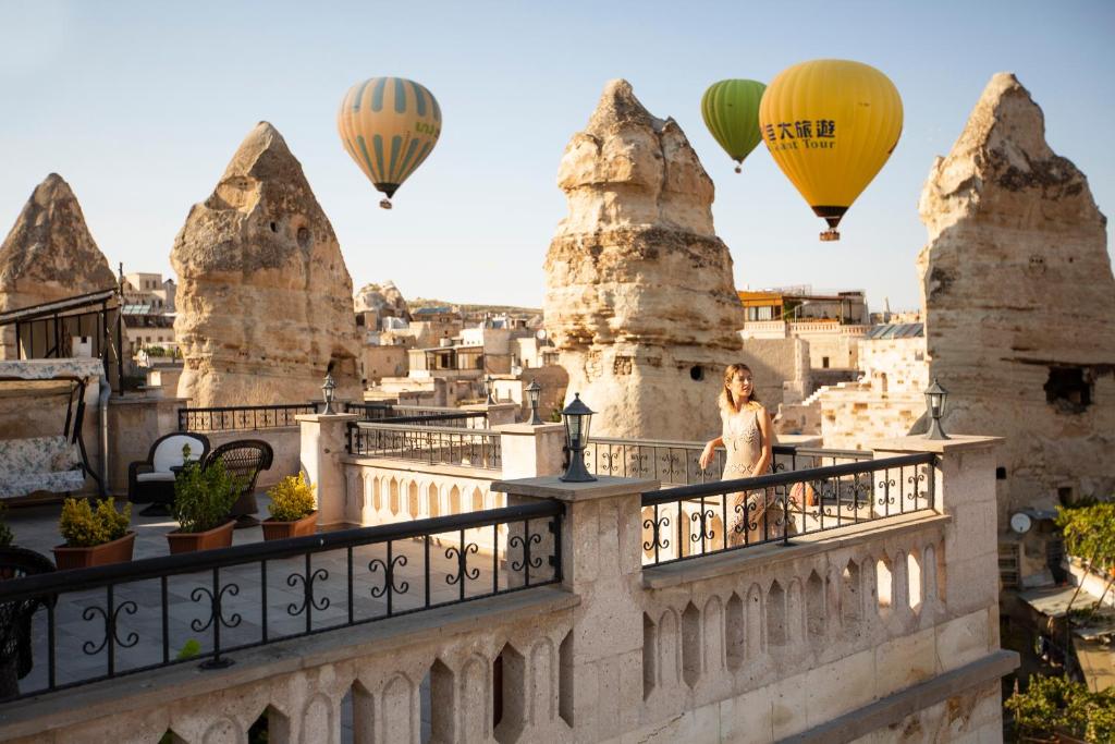 uma mulher de pé numa varanda com balões de ar quente em Stone House Cave Hotel em Goreme