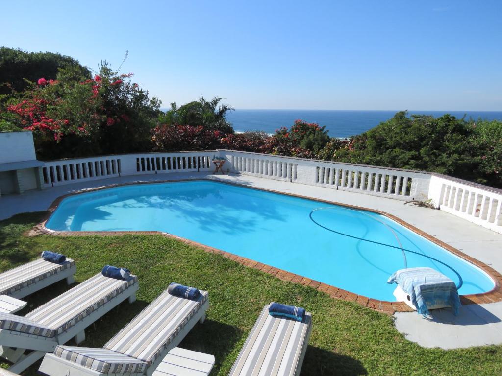 a large swimming pool with two lawn chairs and a fence at Bare Feet Retreat in Scottburgh