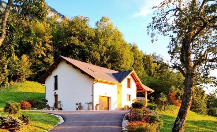 une petite maison blanche sur une route arborée dans l'établissement Gîte Au Coeur Du Noyau, à Aiguebelette-le-Lac