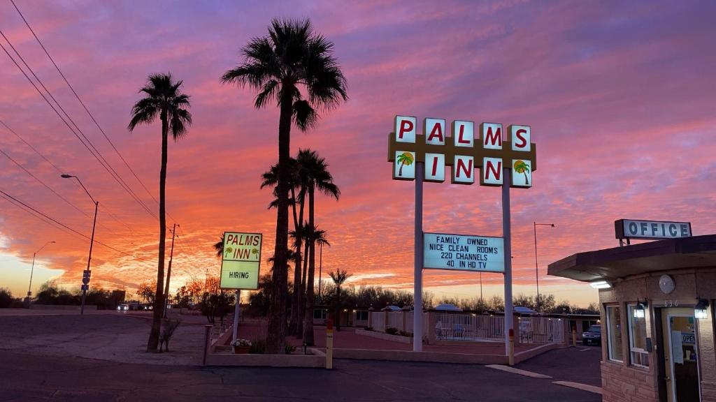 a parking lot with palm trees and a neon sign at Palms Inn in Gila Bend