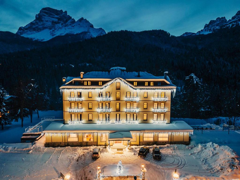 a hotel in the snow with mountains in the background at Hotel Marcora & Spa in San Vito di Cadore