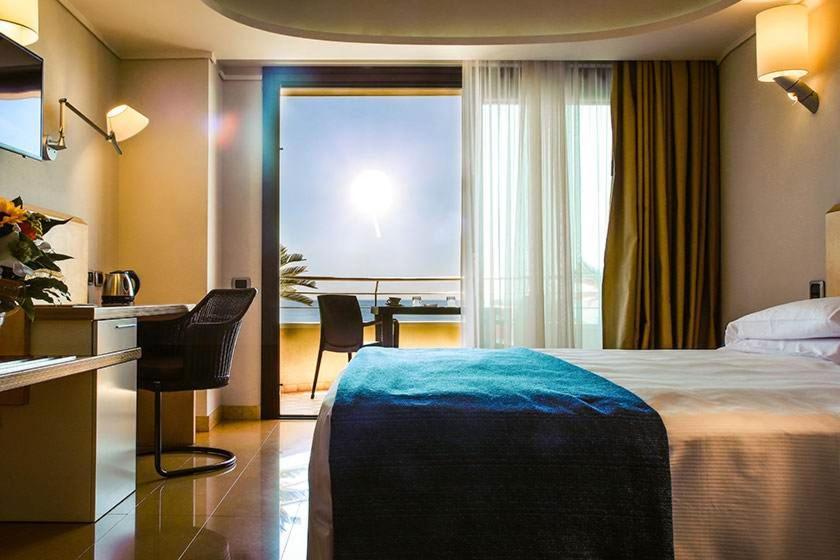 a hotel room with a bed and a desk and a window at Taormina Panoramic Hotel in Taormina