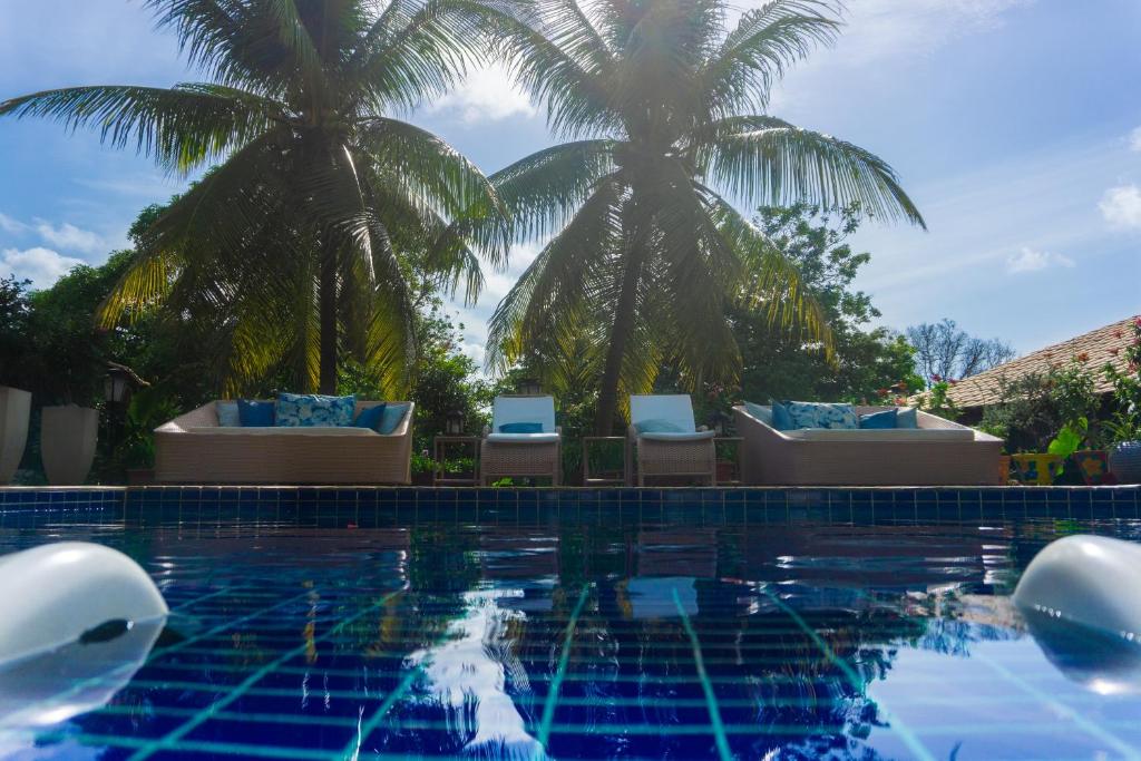 a swimming pool with palm trees and lounge chairs at Xamã Senses - Hotel Pousada in Pipa