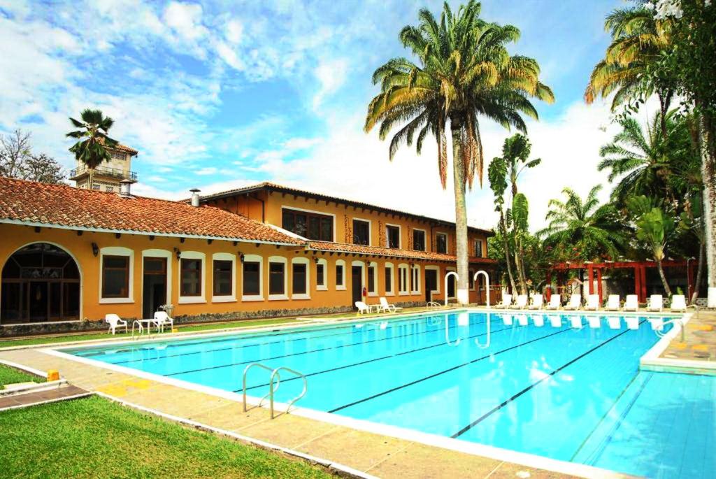 a swimming pool in front of a building with palm trees at Hotel Guadalajara in Buga