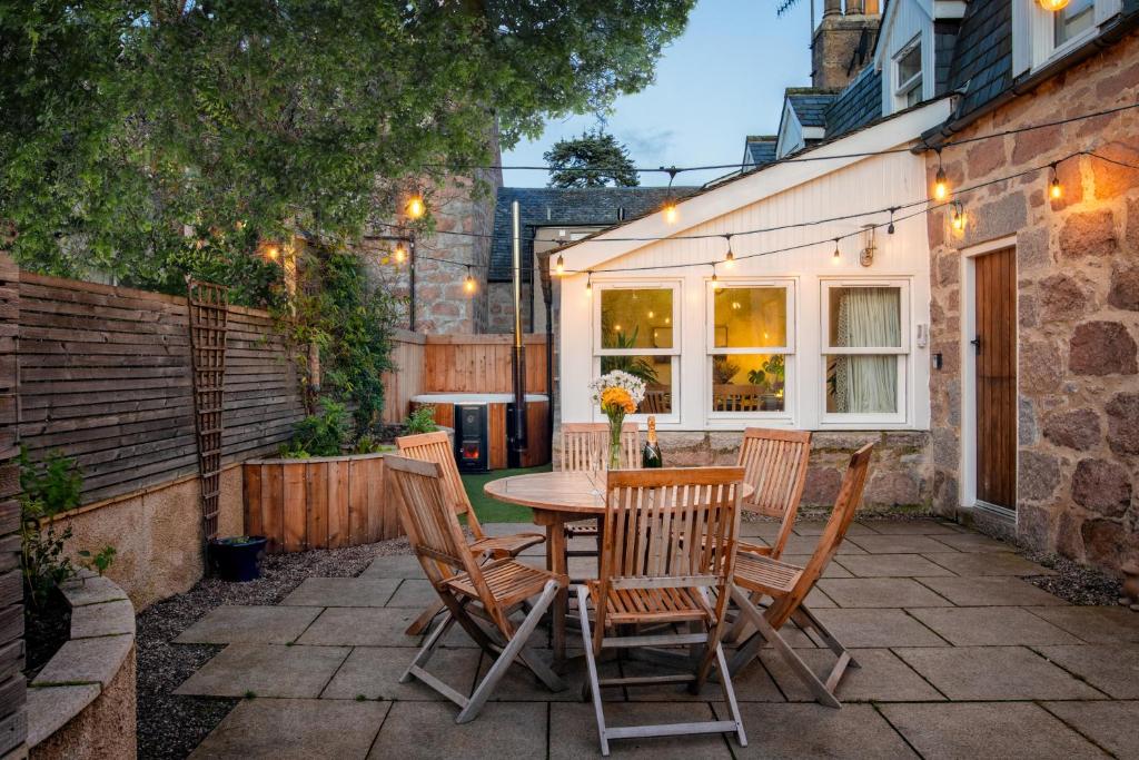 un patio con tavolo, sedie e un edificio di Riverside Cottage with wood fired hot tub in Cairngorms a Ballater