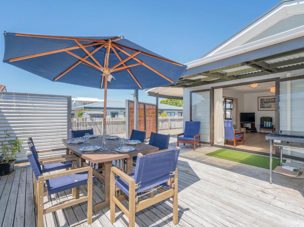 a wooden table and chairs with an umbrella on a deck at Shore Beats Work - Whangamata Holiday Home in Whangamata