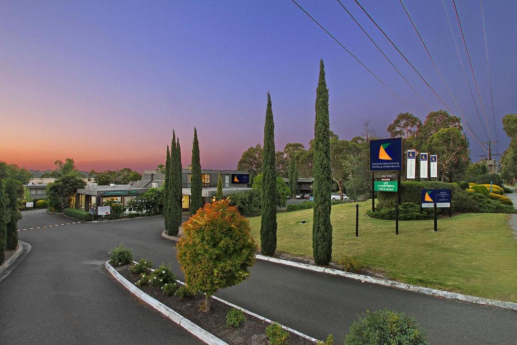 a street with cypress trees and a building at Knox International Hotel and Apartments in Wantirna