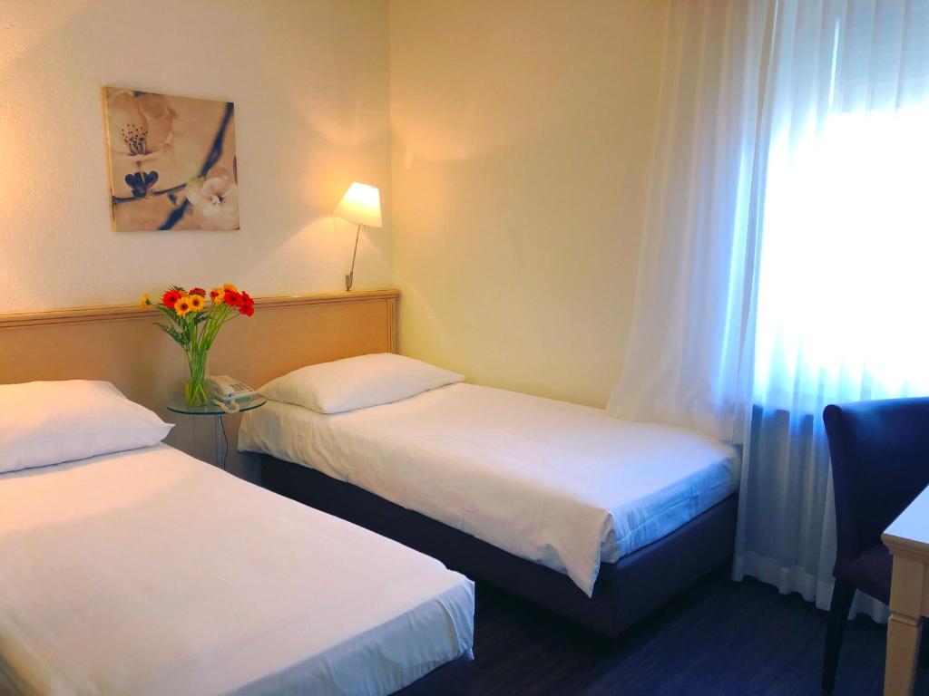 a hotel room with two beds and a vase of flowers at Hotel Neufeld in Zürich